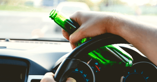 person driving a car while drinking out of alcohol bottle