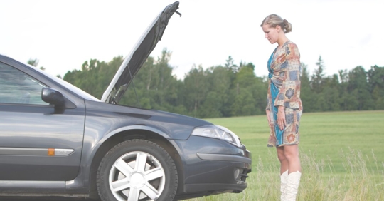 woman looking underneath hood of car