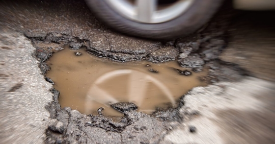 close up image of a car swerving around a pothole in the road